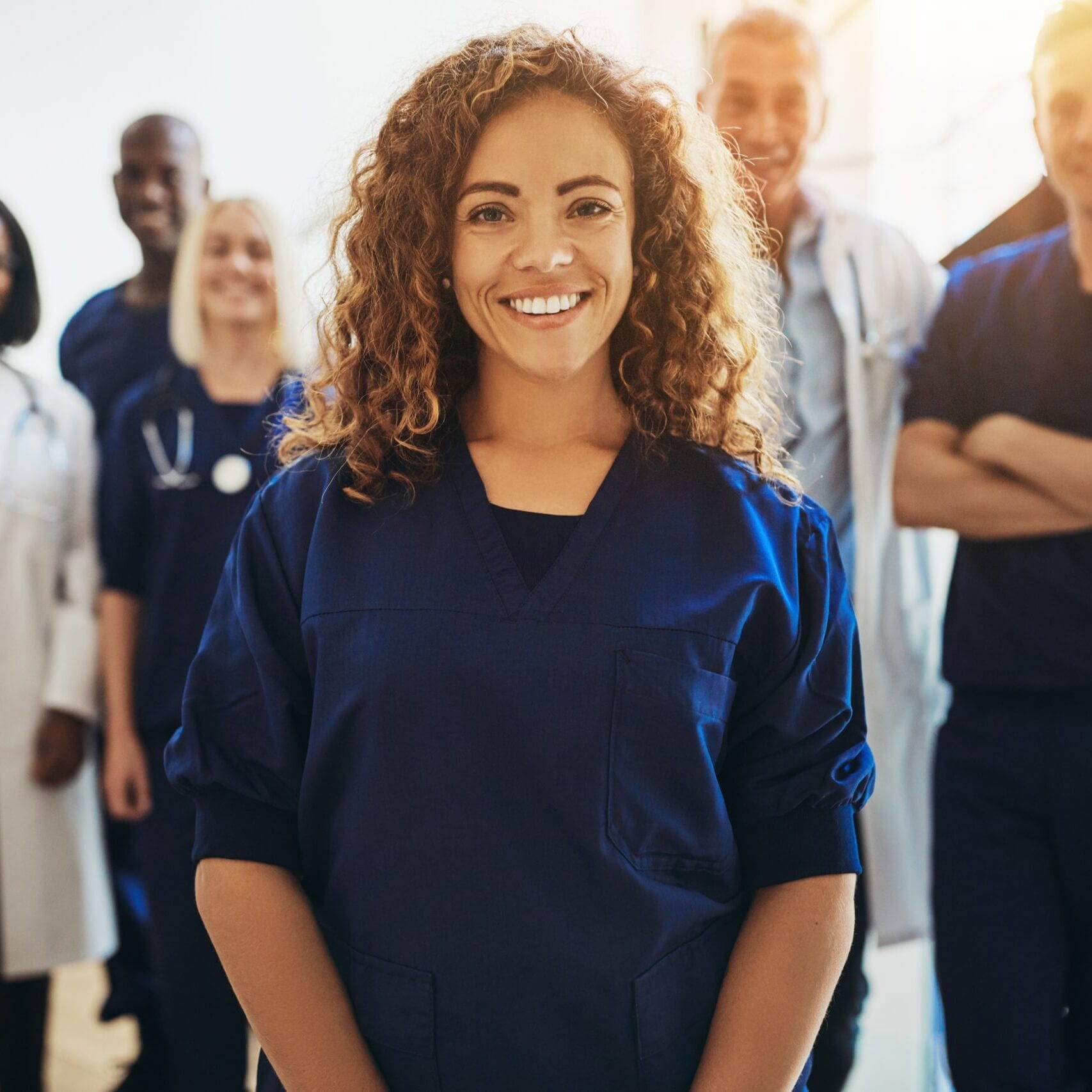 Smiling young female doctor standing in a hospital corridor with a diverse group of medical staff standing behind her